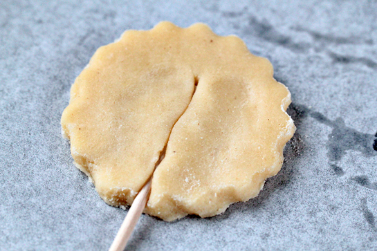 Pie pops recipe with step by step pictures. Line a baking sheet with parchment paper, Place the dough circle onto the sheet. Press down a lollipop stick or a wooden skewer in the dough. Pinch the dough a little to cover the stick.